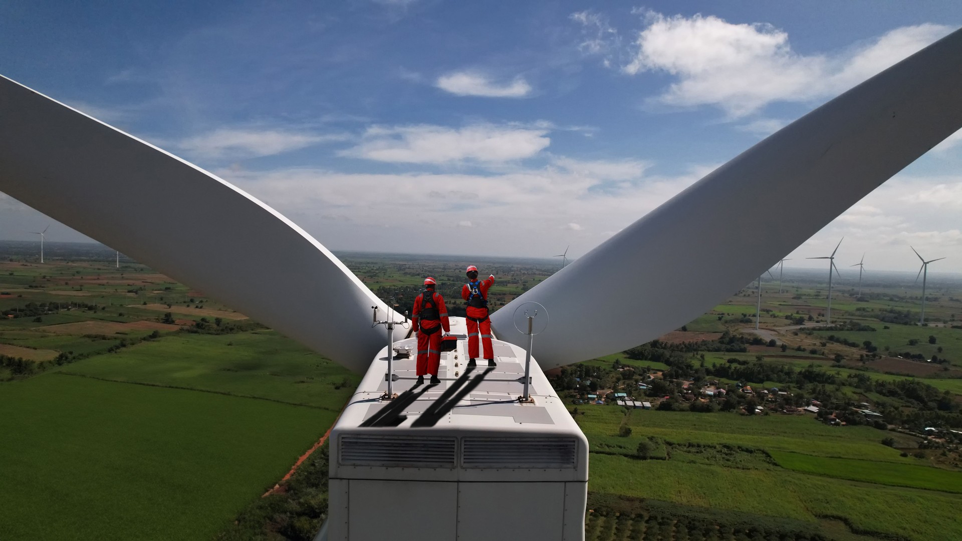 Wind turbine farm, Wind turbine technician and engineer with red safety uniform working on the windmill